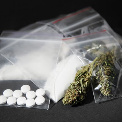 a pile of small plastic bags containing white powder, white pills and dry green leaves